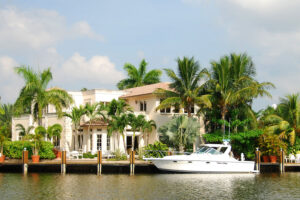 Large Florida house on a canal, with palm trees and a docked boat.