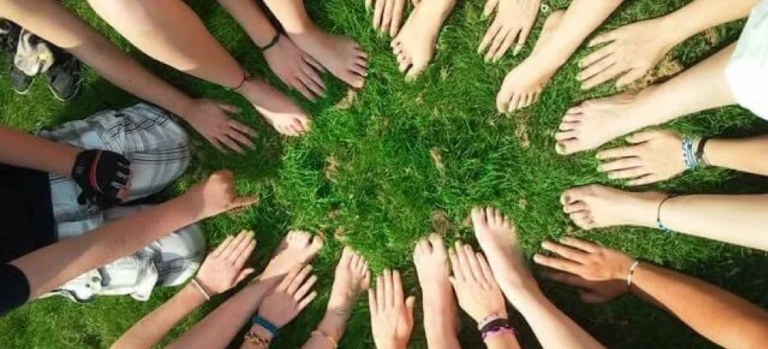 A group of people in a circle placing their hands and feet in the grass