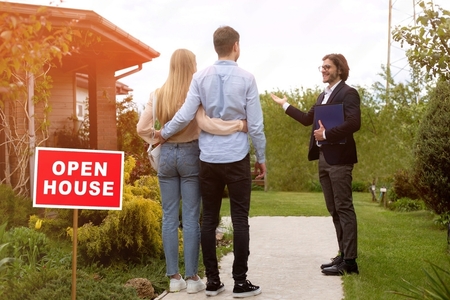 Real estate manager showing open house to young couple outside