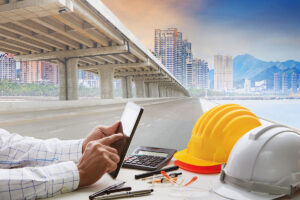 person holding tablet next to hard hats and pencils